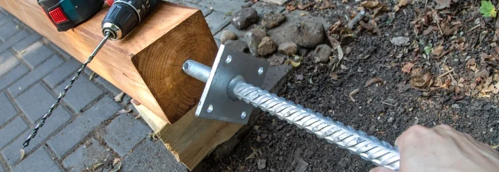 Person befestigt einen Metallanker an einem Holzbalken